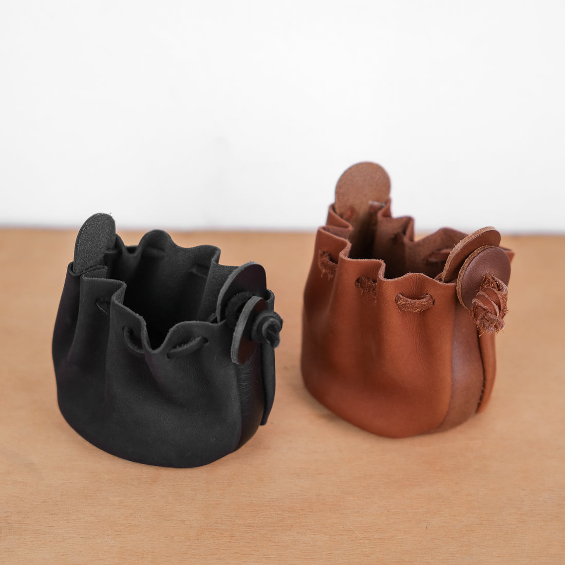 Deux bourses cuir souple noir et cognac côte à côte, coloris comparés, fermeture cordon, 8 x 10 cm